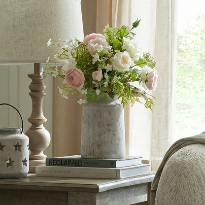 Bloomville Urn Stone Vase holding pink and white flowers on books beside a lamp and window