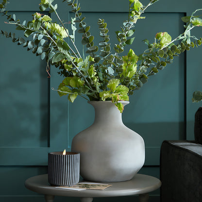Darcy Squat Stone Vase holding leafy stems on a round table against teal panelling