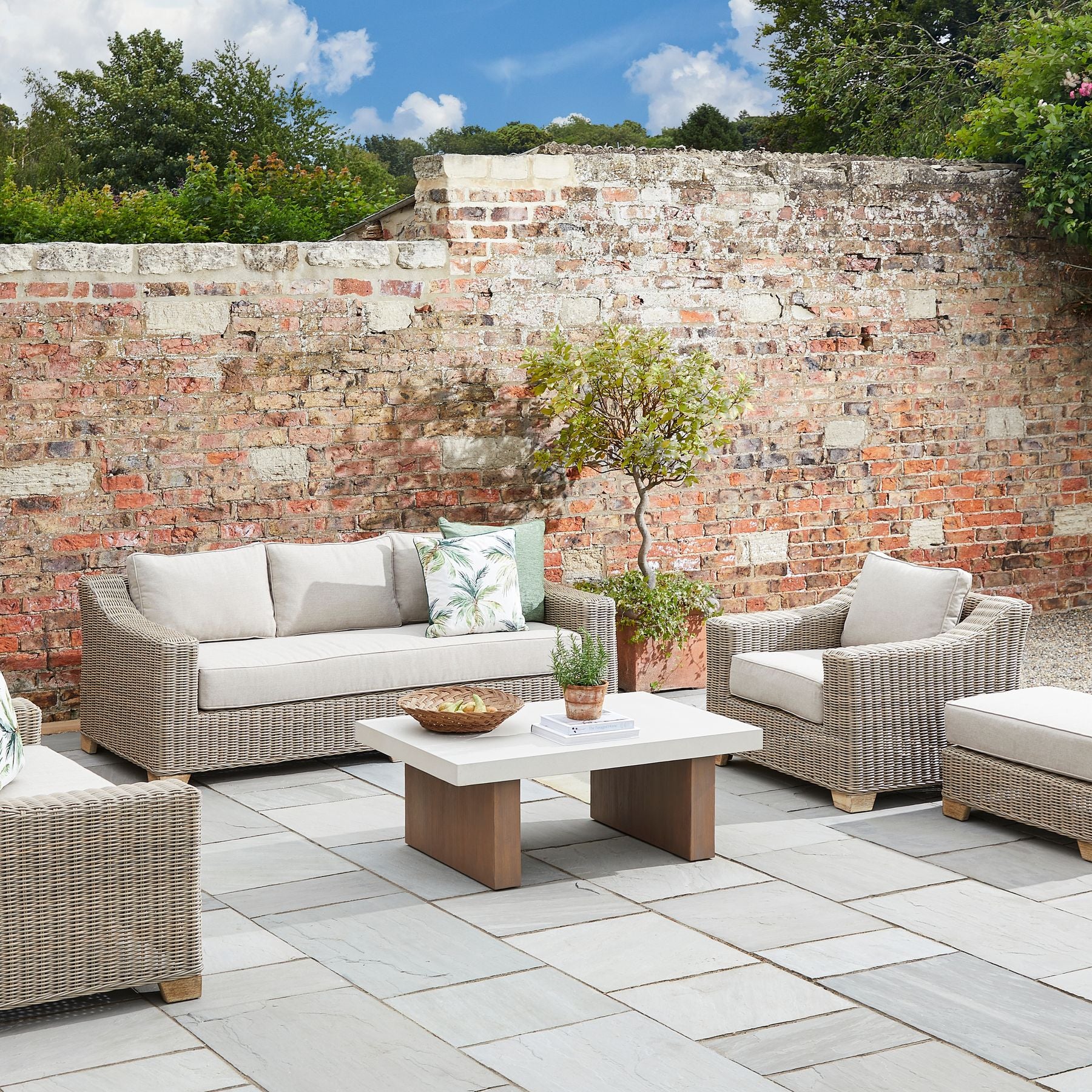 Capri Collection outdoor rattan armchair with cream cushions, weather-resistant wicker garden lounge chair styled on stone patio