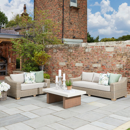 Capri Collection outdoor two seater rattan sofa with cream cushions, weather-resistant wicker garden lounge set styled on stone patio