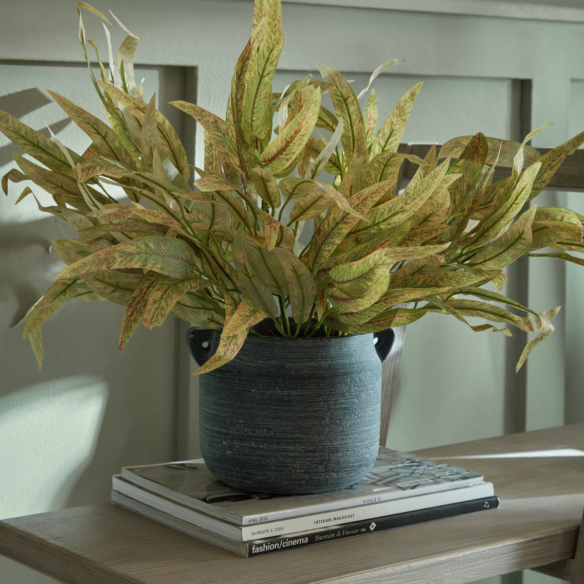 Amalfi Grey Hydria Pot styled with leafy stems on stacked books against a panelled wall