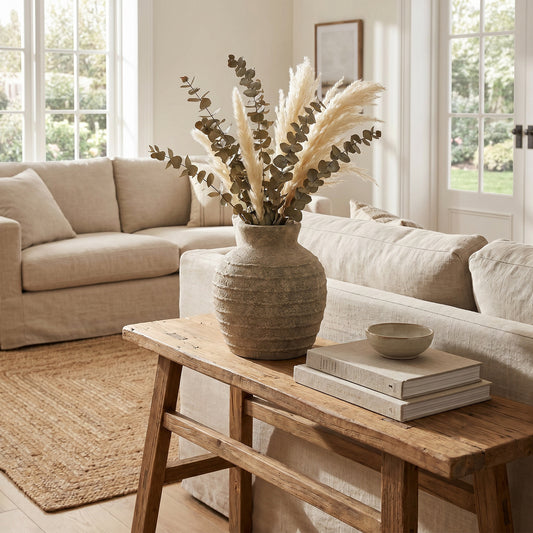 Large Tuscan Grey Vase with foliage and pampas-style stems on a wooden console behind a pale sofa