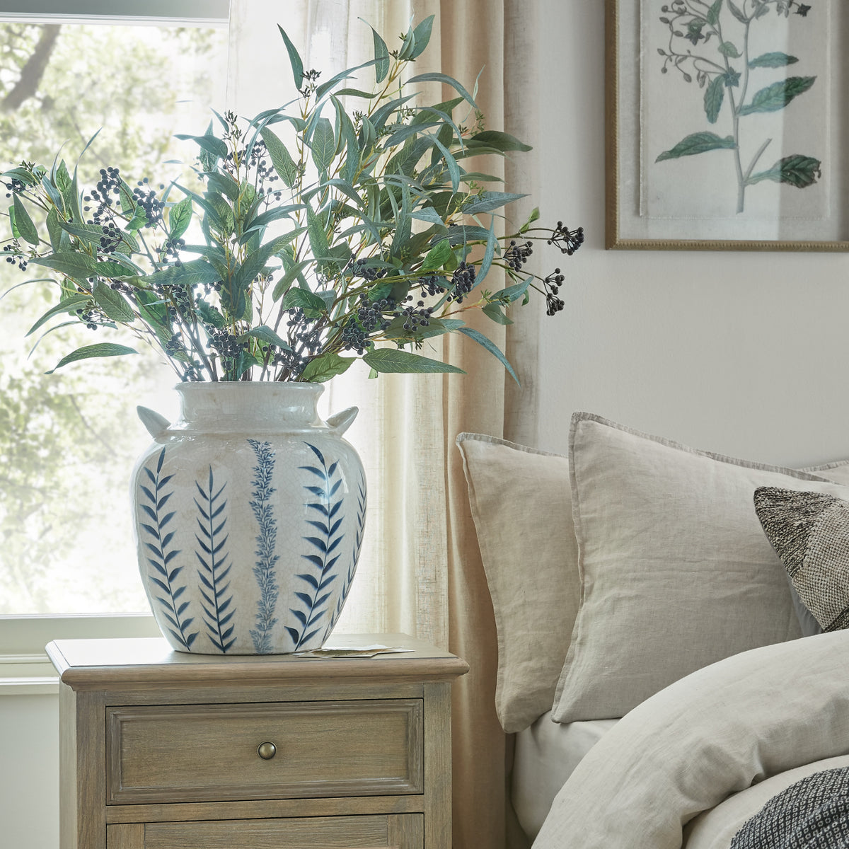 Blue Flora Amphora Vase with foliage on a bedside table beside a window